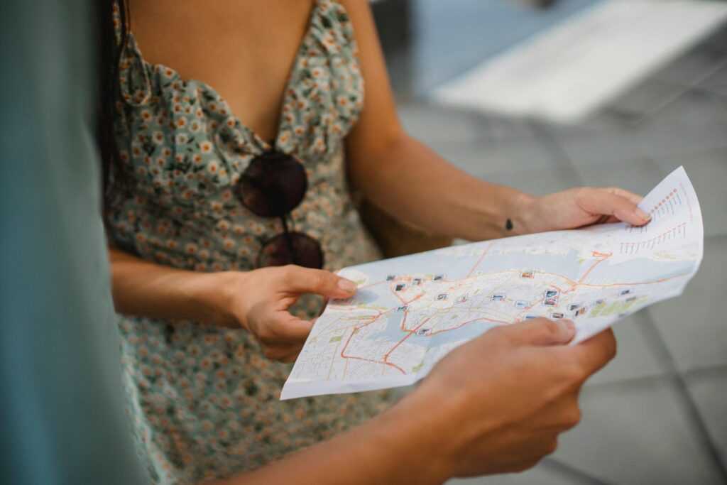 Crop anonymous couple travelers in summer clothes checking location in paper map while walking in unknown city