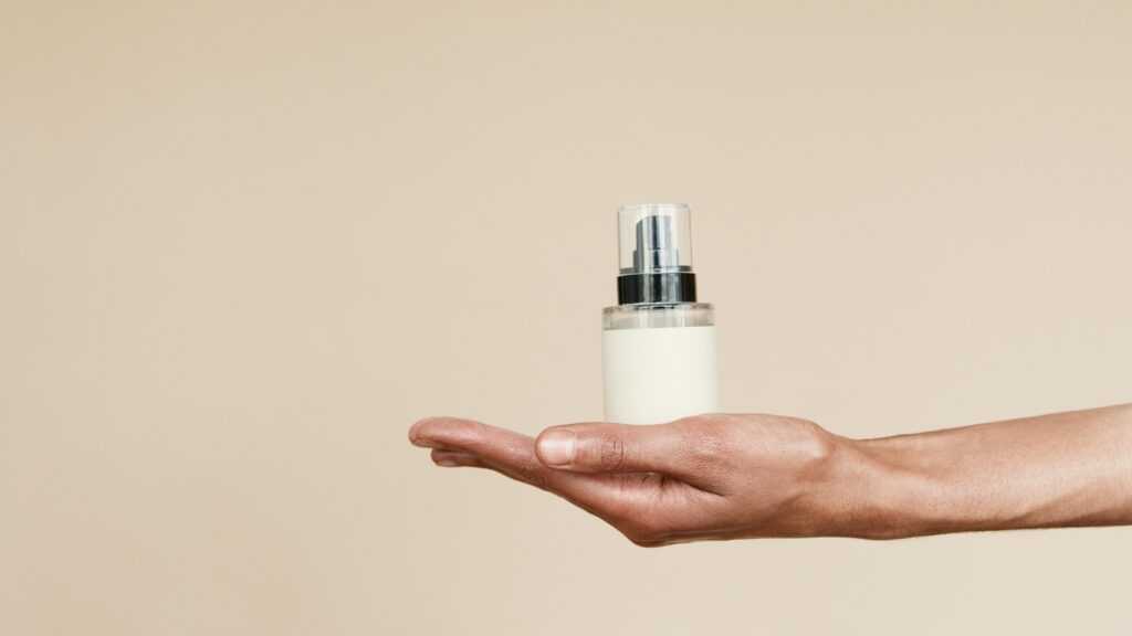 Elegant close-up of a hand holding a perfume bottle against a neutral background, perfect for product display.