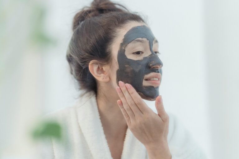 A woman in a bathrobe applies a charcoal beauty mask, promoting skincare and relaxation.